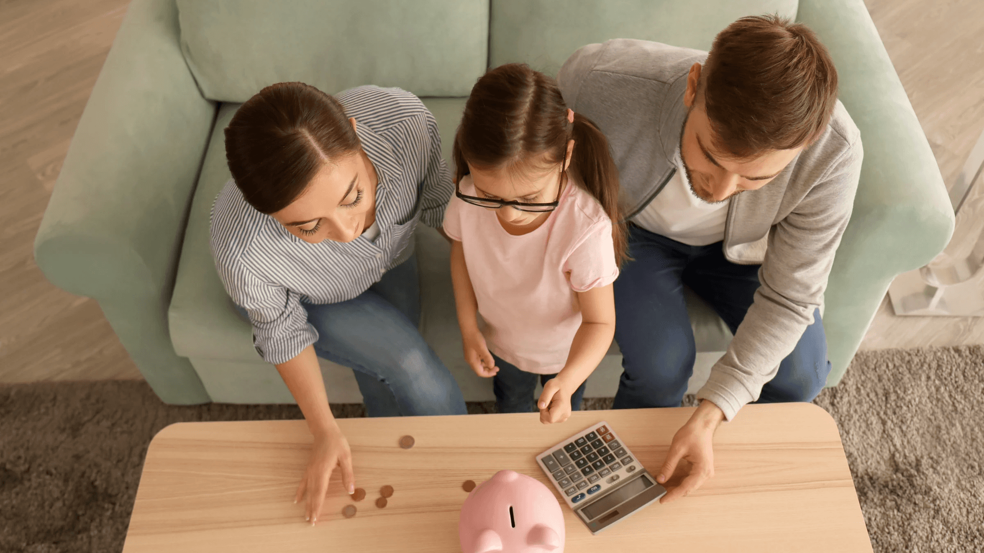 Familia contando monedas en la mesa del salón, con una hucha de cerdito y una calculadora.