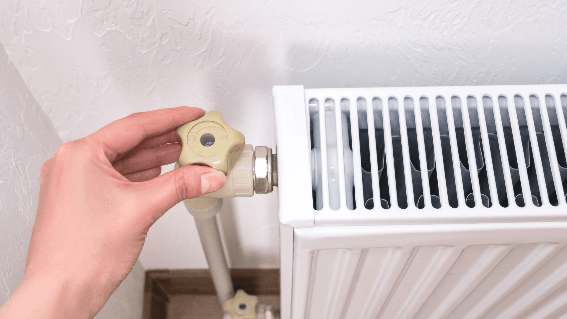 Mano girando la llave termostática de un radiador blanco de calefacción.