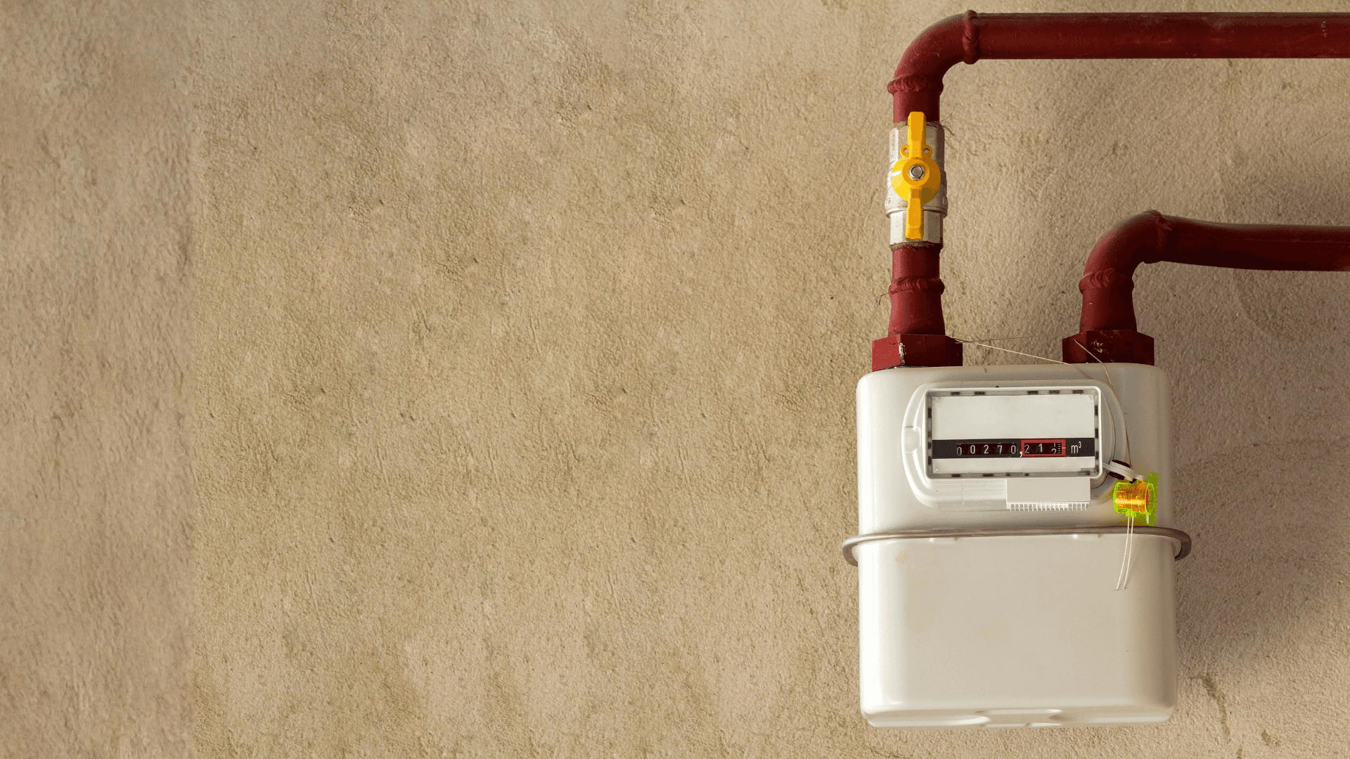 Contador de gas natural instalado en una pared, con sus tuberías rojas y la llave de paso amarilla.