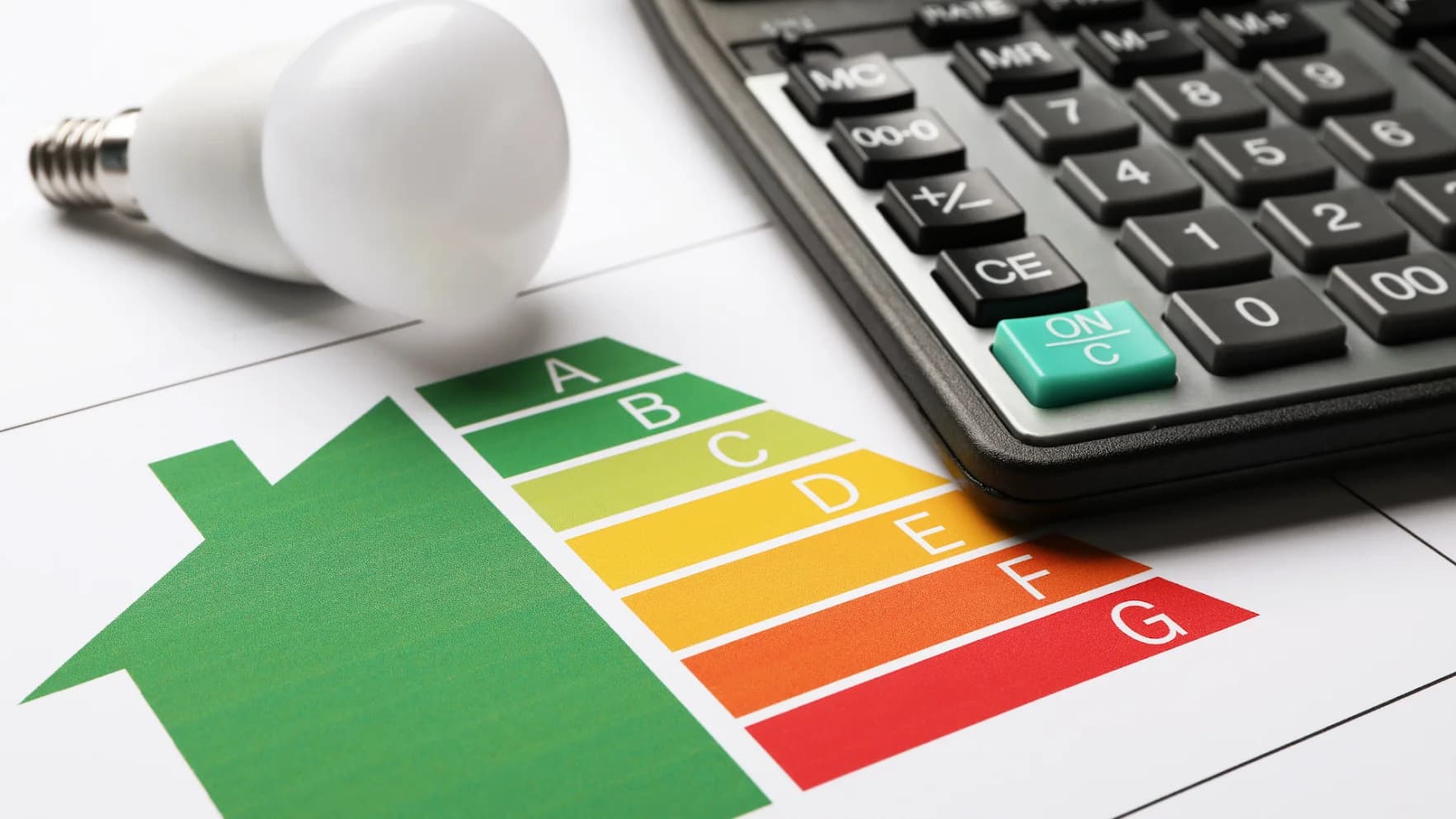 Persona sujetando una bombilla sobre montones de monedas junto a una calculadora, calculando el consumo eléctrico de su casa.