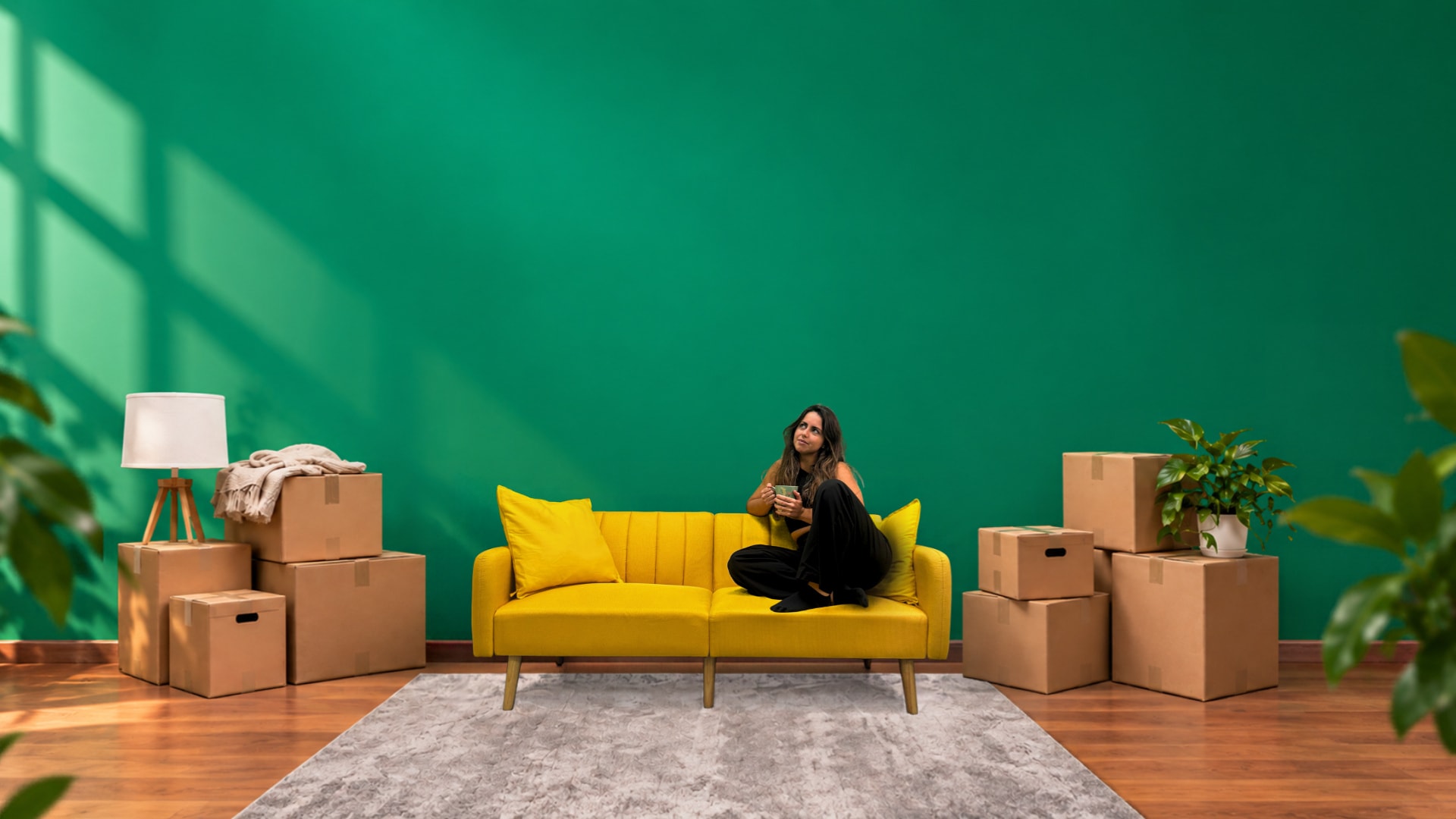 Una mujer con un café descansa en un sofá amarillo, en un salón con las cajas de la mudanza aún sin abrir